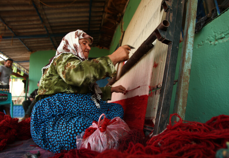 赤く草木染めされた糸を紡ぐ女性の写真