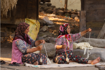 糸紡ぎ用のコマを使い手で糸を紡いでいる女性二人の写真